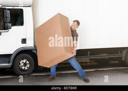 Un uomo di consegna o Mover Holding scatola pesante nella parte anteriore del furgone Foto Stock