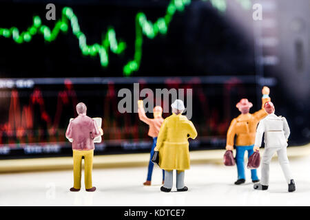 Il concetto di business, primo piano delle figurine in miniatura di uomini di affari in piedi di fronte a grande schermo sfocati con prezzo di stock market grafico con indicatore Foto Stock