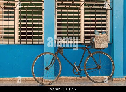 Vecchia bicicletta appoggiata contro bloccate,finestre con persiane e parete blu Foto Stock