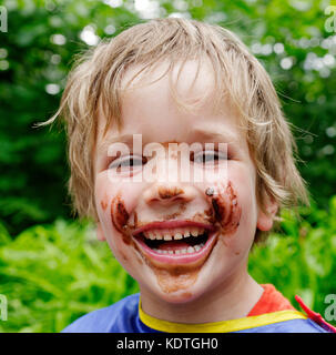 Un piccolo ragazzo (5 anni) di ridere con il suo volto ricoperto di cioccolato dopo mangiare un gelato al cioccolato Foto Stock