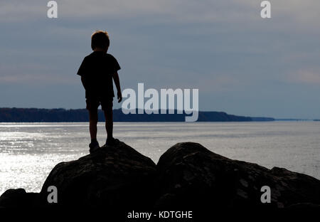 Un ragazzino(5 anni) profilarsi in piedi su rocce sulla St Lawrence river shore a Cap Rouge vicino a Quebec City, in Canada Foto Stock