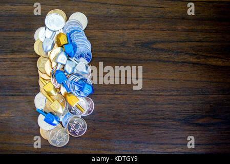 Pila di colorate hanukkah monete e dreidels su un marrone tavolo in legno con spazio di copia Foto Stock