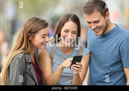 Tre amici felice controllo smart phone contenuto in piedi fuori in strada Foto Stock