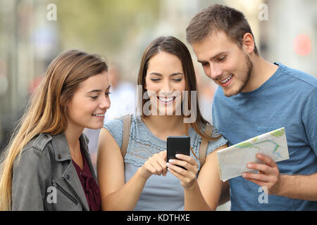 Tre turisti posizione di controllo utilizzando una mappa su carta e uno smart phone su strada Foto Stock
