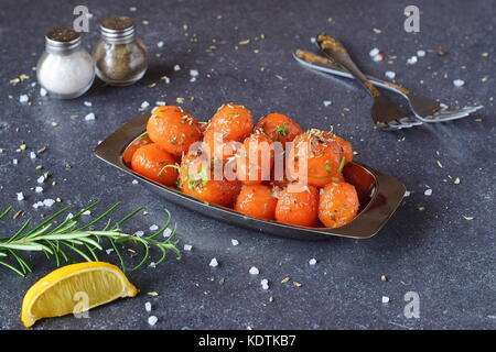 Glassato al miele carotine con sale marino e timo in un recipiente di metallo posto su un grigio Sfondo astratto. Il mangiare sano concetto. fissaggio di cibo. pasto sano. Foto Stock