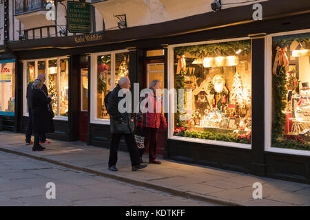 Serata in centro di York e persone che camminano giù Stonegate sono attratti dal Natale illuminato la finestra di visualizzazione in uno storico negozio di fronte - Inghilterra, Regno Unito. Foto Stock