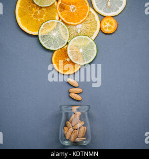 Cibi sani e il concetto di medicina. Bottiglia di vitamina C e di vari agrumi. mixed agrumi fettine di lime,arancio e limone su sfondo grigio Foto Stock