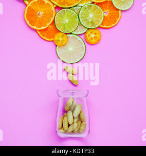 Cibi sani e il concetto di medicina. Bottiglia di vitamina C e di vari agrumi Agrumi fettine di lime,arancio e limone su luce sfondo rosa Foto Stock