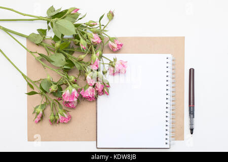 Mockup con Blocco note di vuoto e piccolo giardino di rose rosa. area di lavoro. Foto Stock
