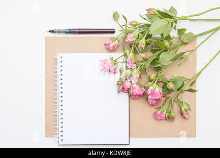 Mockup con Blocco note di vuoto e piccolo giardino di rose rosa. area di lavoro. Foto Stock