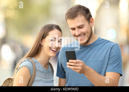 Coppia felice godendo utilizzando uno smart phone permanente sulla strada Foto Stock