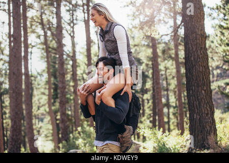 Escursionismo coppia avendo divertimento mentre trekking nella foresta. Equitazione donna piggyback sull'uomo durante le escursioni nella foresta. Foto Stock