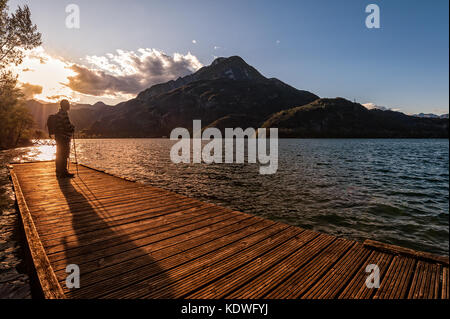 Escursionista in piedi sul dock fine sul lago. Tramper guardando il tramonto sul lago. Foto Stock