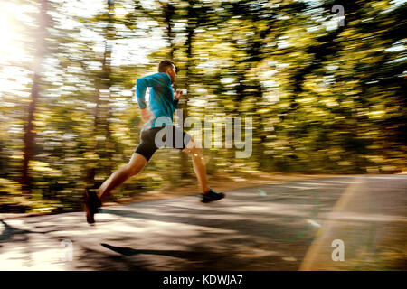 Sfocata maschio moto runner in esecuzione su strada forestale in presenza di luce solare Foto Stock