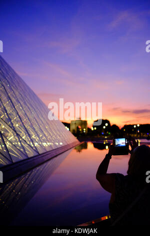 Un turista prende una foto del Louvre di notte a Parigi, utilizzando il suo smartphone Foto Stock