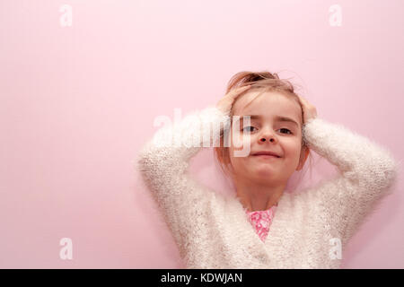 Di piccole dimensioni e di colore bianco caucasico ragazza bionda bambino le mani sulla testa tirando hari pianura sfondo rosa Foto Stock