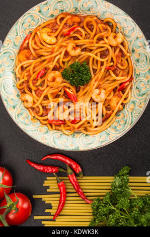 Stile italiano piccante di gamberi o gamberetti spaghetti in un peperoncino Salsa di pomodoro su sfondo nero Foto Stock