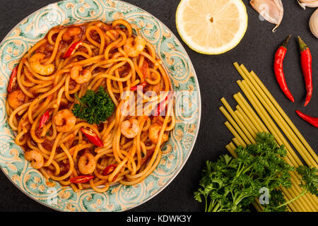 Stile italiano piccante di gamberi o gamberetti spaghetti in un peperoncino Salsa di pomodoro su sfondo nero Foto Stock