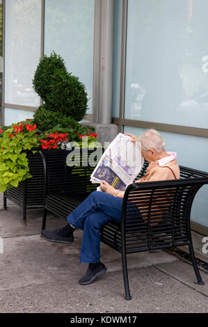 Donna anziana senior seduta su una panchina leggendo un giornale, Vancouver, BC, Canada Foto Stock