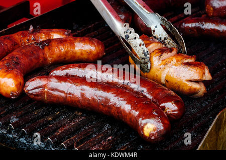 Salsicce bratwurst su ghisa piastra. pinze in metallo. Foto Stock