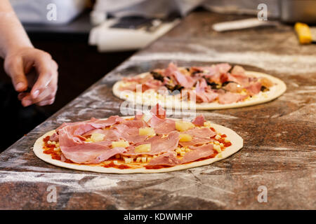 Cuocere mettendo condimenti su due pizze. Foto Stock