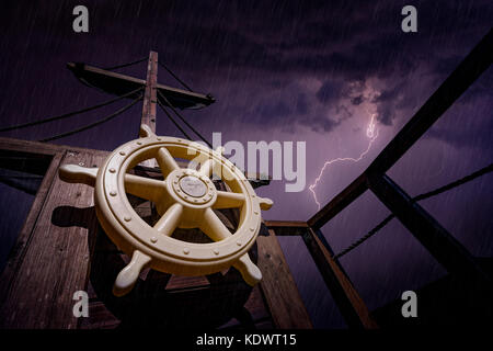 Il volante e il montante in legno di una nave pirata durante la tempesta con cielo tempestoso e alleggerire in background Foto Stock