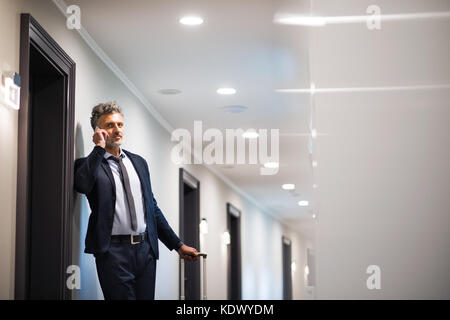 Imprenditore maturo con lo smartphone in un hotel corridoio. uomo bello stare in un hotel corridoio, facendo una telefonata. Foto Stock