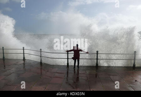 Una donna si brace mentre le onde si infrangono sul muro di mare a Penzanze, in Cornovaglia, mentre l'uragano Ophelia colpisce il Regno Unito e l'Irlanda con raffiche fino a 80 mph. Foto Stock