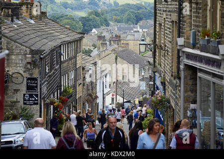 Pennines village, Haworth nel West Yorkshire, Inghilterra. I turisti si mescolano sulla strada principale di una ripida strada basolata foderato con interessanti negozi Foto Stock