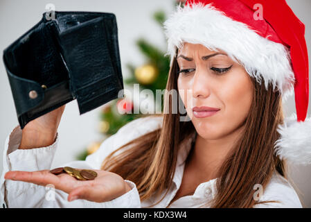 Ritratto di una giovane bella imprenditrice che indossa santa hat e guarda con tristezza al portafoglio vuoto. Foto Stock