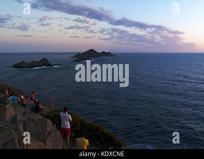 Corsica: la gente guardando il tramonto sull'Iles Sanguinaires (sanguinosa isole), quattro famosi rosso scuro isole di porfido con un faro risalente 1844 Foto Stock