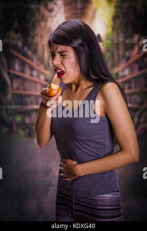 E bella ragazza solitaria sofferenza da anorexy, sofferenza dolore nel suo stomaco mentre lei sta mangiando un Apple, in uno sfondo sfocato Foto Stock