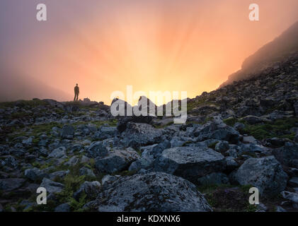 Uomo in piedi davanti alla luce del sole in una serata estiva in montagna lofoten island Foto Stock