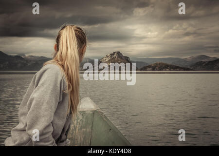 Donna traveler sulla vela barca verso la riva con con montagne paesaggio sull orizzonte in giorno nuvoloso con drammatica sky Foto Stock