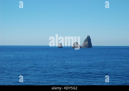 Un cluster di tre scogli passando da un blu scuro oceano. L'acqua è calma. il cielo è blu, con assenza di nubi. Foto Stock