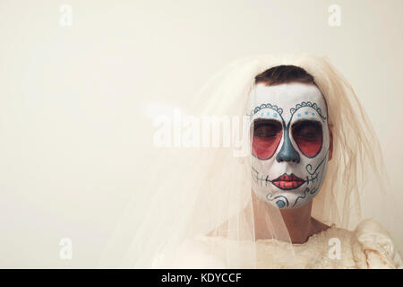 Primo piano di una persona con capelli corti in un abito da sposa con un messicano calaveras trucco, indossando il velo contro un fondo bianco con uno spazio vuoto Foto Stock