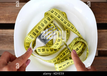 Concetto di dieta con la donna pronti a mangiare un nastro di misurazione dalla piastra bianca usando il coltello e la forchetta, perdere peso per ottenere montare Foto Stock