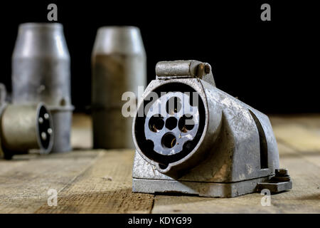 Vecchia spina e presa alta tensione. vecchi accessori elettrici. tavolo in legno, sfondo nero Foto Stock