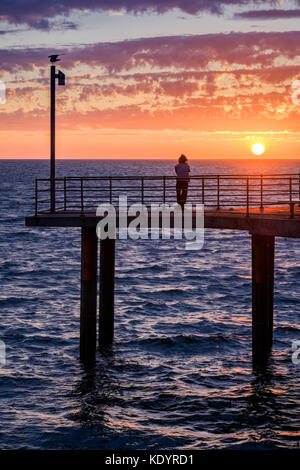 Un lone persona gode di un magnifico tramonto al mare di Adelaide del molo di Brighton su una mite serata d'estate. Foto Stock
