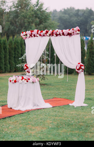 La composizione di nozze di nozze arch e tavolo decorato con fiori colorati e perle pendenti. Foto Stock