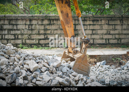 Organge pesante escavatore con pala in piedi sulla collina con rocce Foto Stock