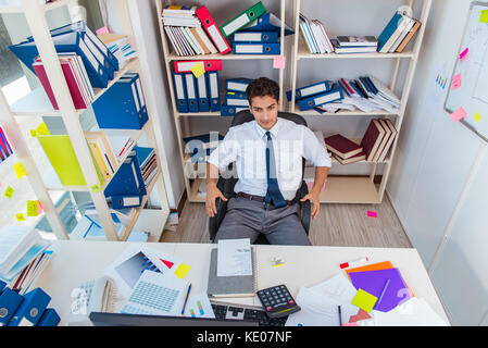 Imprenditore lavora in ufficio con pile di libri e giornali facendo di documenti cartacei Foto Stock