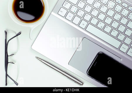 Vista ravvicinata di still life con computer portatili e smartphone, penna e bicchieri accanto a una tazza di caffè su sfondo bianco Foto Stock