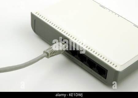Vista ravvicinata di grigio di un cavo LAN è collegato a un router con gli slot vuoti su sfondo bianco Foto Stock