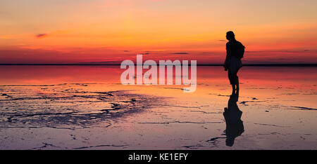 Silhouette di un solo uomo che guarda verso la vibrante tramonto riflesso in acque poco profonde di solt lago Foto Stock