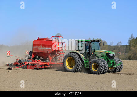 Salo, Finlandia - 8 maggio 2016: John Deere 6125r trattore agricolo e horsch seminatrice sul campo polveroso a molla con cielo blu. Foto Stock