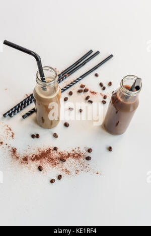 Due bottiglie di vetro con caffè freddo cocktail e cannucce, i chicchi di caffè e di cacao in polvere isolata su bianco Foto Stock