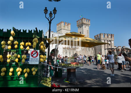 Sirmione, Italia. vista colorate di frutta fresca dal fornitore con l'ingresso al castello scaligero in background. Foto Stock