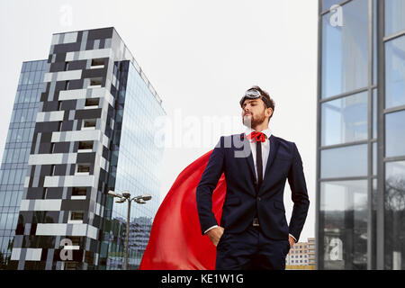 Un imprenditore in un costume da supereroe si erge contro un edificio b Foto Stock