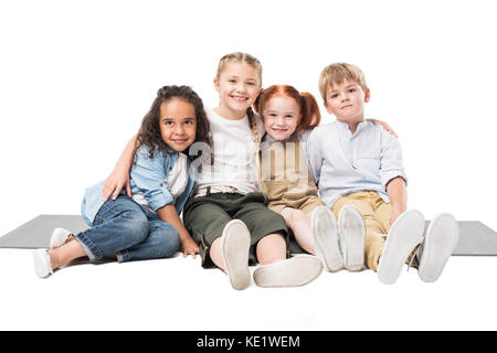 Felice multietnica bambini seduti insieme isolato su bianco